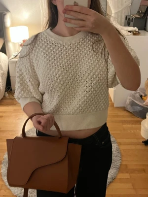 Vit stickad cropped tröja - Snygg vit stickad cropped tröja med strukturmönster och breda ribbade muddar vid ärmslut och midja. Tröjan har rund halsringning och kortare passform, perfekt att styla med höga jeans. Materialet är mjukt och bekvämt.