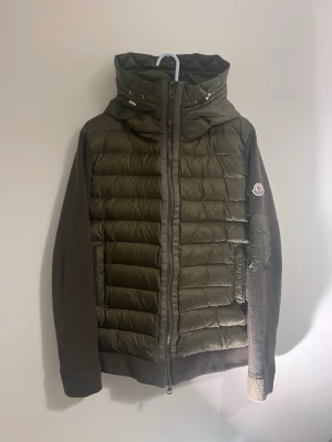Olivgrön cardigan från Moncler - Säljer en olivgrön pufferjacka från Moncler med stickade ärmar och huva. Jackan har dragkedja framtill, quiltad framsida och en ficka med dragkedja på ärmen.  Storlek M-L passar 180-190. Fattas knap på insidan till fikan men fungerar utanproblem. Finns tecken på användning men mycket liv kvar 👏Skriv vid frågor eller bilder | byten är accepterade