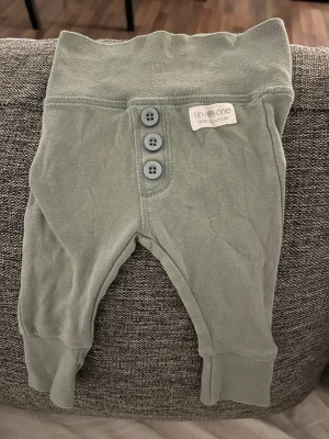 Bebis kläder Gröna babybyxor från Tiny One - Supersöta ljusgröna babybyxor från Tiny One i mjuk ekologisk bomull. Byxorna har bred mudd i midjan, fyra dekorativa knappar framtill och ribbade benslut för extra komfort. Perfekta för de allra minsta!