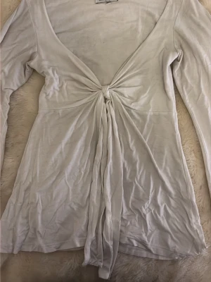 Vit omlottopp från Design by Si - Säljer en vit omlottopp från Design by Si i storlek XS/S. Toppen har lång ärm, djup v-ringning och knyt framtill. Tillverkad i mjuk bomull som känns skön mot huden. 