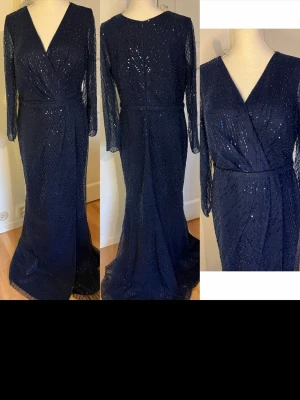 NY Marinblå glittrig långklänning / balklänning  - Säljer en marinblå långklänning med glittriga paljetter och omlott överdel. Klänningen har v-ringning, långa transparenta ärmar och en lätt slits framtill. Perfekt för bal eller festliga tillfällen. Materialet känns som polyester med meshdetaljer.