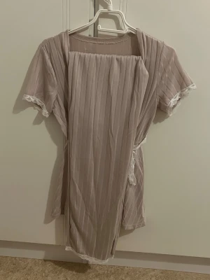 Beige omlott pyjamas med spetsdetaljer - Säljer en beige omlott pyjamas set med tunna vertikala ränder och knytband i midjan. Överdelen har v-ringad hals och spetsdetaljer vid ärmslut. Materialet känns mjukt och flowy, säljer pågrund av underdelen är för lång för mig har aldrig använt bara provat