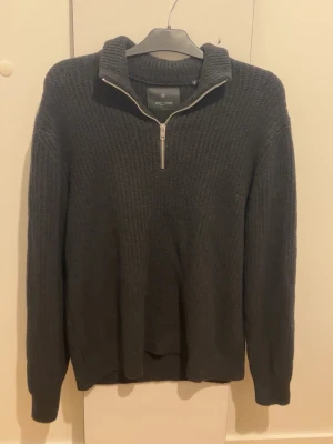 Svart stickad tröja från Jack & Jones - Mysig svart stickad tröja från Jack & Jones med hög krage och half zip-dragkedja. Tröjan har en chunky struktur och långa ärmar, perfekt för kyliga dagar. Enkel och stilren design som funkar till det mesta.