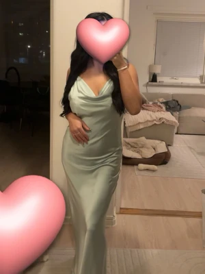 Ljusgrön långklänning med smala band - Säljer en elegant ljusgrön långklänning med smala axelband och draperad urringning. Klänningen har en figurnära passform och är tillverkad i ett glansigt, mjukt material som ger en lyxig känsla. Perfekt för speciella tillfällen. 