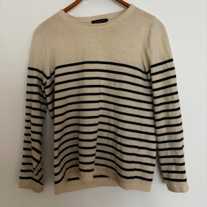 Randig tröja från Bruuns Bazaar - Snygg beige tröja från Bruuns Bazaar med svarta horisontella ränder. Tröjan har rund halsringning och långa ärmar. Perfekt för en avslappnad och stilren look. Materialet känns mjukt och bekvämt mot huden.
