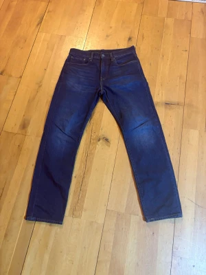Levi's 502 mörkblå jeans W31 L32 - Säljer ett par Levi's 502 jeans i mörkblå tvätt. Klassisk femficksmodell med raka ben och normal passform. Jeansen har snygga slitningar och är tillverkade i tåligt denimtyg av bomull. Perfekta för dig som gillar tidlös stil och kvalitetskänsla.