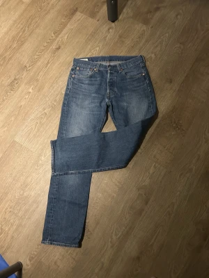 Levi's Premium 501 blå jeans - Klassiska Levi's Premium 501 jeans i blå tvätt. Rak passform med fem fickor och knappgylf. Jeansen har den ikoniska läderlappen bak i midjan och röda Levi's-taggen på bakfickan. Tillverkade i slitstarkt bomullsjeansmaterial.