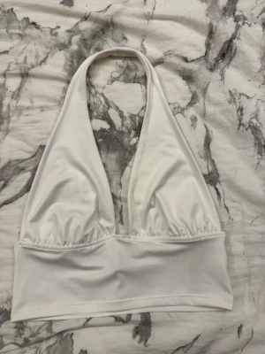 Vit halterneck topp från H&M Divided - Säljer en vit halterneck topp från H&M Divided i storlek M. Toppen har en djup urringning och bred resår under bysten för extra stöd. Tillverkad i mjukt och stretchigt material som känns skönt mot huden. Perfekt till sommaren och enkel att styla.
