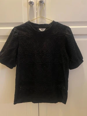 Svart blus - Säljer en svart blus med korta ärmar och spetsmönster. Blusen har rund halsringning och passar perfekt till både jeans och kjol !