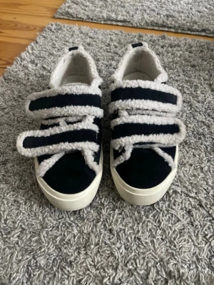 Svarta sneakers med fluff från Inuikii - svarta sneakers från Inuikii med tjock vit sula och fluffiga, breda kardborren och kanter. Skorna har en cool kontrast mellan svart tyg och vita, lurviga detaljer som ger en trendig look. Perfekta för dig som vill sticka ut med din stil.