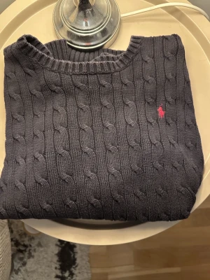 🖤 Polo Ralph Lauren kabelstickad tröja - tröja med ikonisk logga. En riktig garderobsklassiker som aldrig tappar stil. Perfekt till både skjorta och t-shirt – elegant, sportig och tidlös på samma gång.