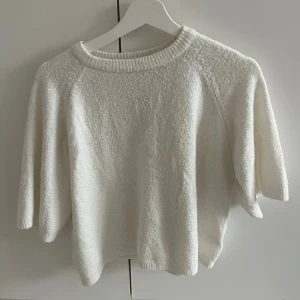 Vit stickad tröja med kort ärm - Säljer en vit stickad tröja med rund hals och korta, lite bredare ärmar. Tröjan har en loose passform och är gjord i mjukt material som känns skönt mot huden. Perfekt för dig som gillar en enkel och clean look.