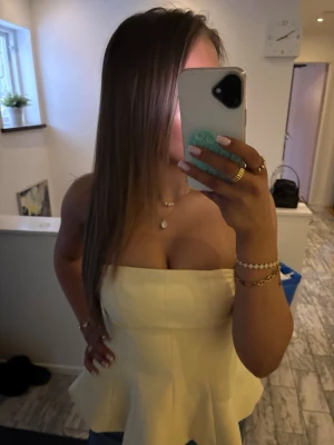 Gul axelbandslös bandeu top - Säljer en söt gul axelbandslös bandeu topp. Toppen har en figurnära passform upptill och volang nertill som ger en snygg siluett. 