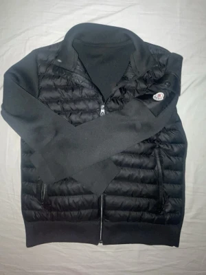 Moncler jacka  - Snygg svart dunväst från Moncler med quiltad front och Moncler-logga på ärmen. Västen har dragkedja framtill och ribbade muddar nedtill. Perfekt för lager-på-lager och ger en clean look till din outfit.  Den är medium men passar Large också.