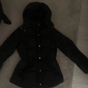 Svart dunjacka med huva - Snygg svart dunjacka med huva och justerbar midja och inbyggd krage innanför jacka.  Funkar både till skidor och vardags 