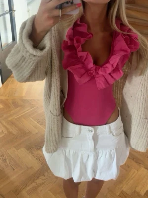 Rosa volang body toppmed djup sopringning💖💖 - Snygg rosa topp med stora volangdetaljer runt den djupa sopringningen. Toppen är ärmlös och har en croppad passform som ger en trendig look. Perfekt att styla med kjol eller jeans för en cool outfit.