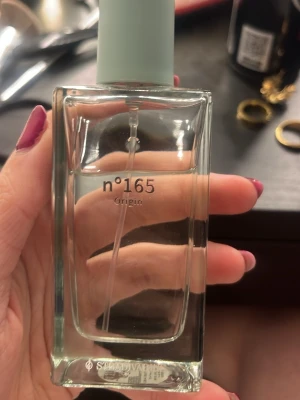 Stradivarius n°165 Origin parfym - Minimalistisk parfymflaska från Stradivarius med doften n°165 Origin. Flaskan är rektangulär i genomskinligt glas och har ett ljusblått lock. Enkel och stilren design som passar perfekt på sminkbordet.