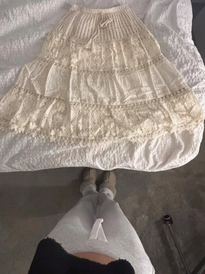 Beige långkjol med spets och volanger - Litet rivsår men syns inte! Romantisk beige långkjol med bred resår i midjan och knytband. Kjolen har flera lager med spetsdetaljer och volanger, samt ett vackert broderat mönster. Perfekt för dig som gillar boho-stil och vill ha något unikt i garderoben.