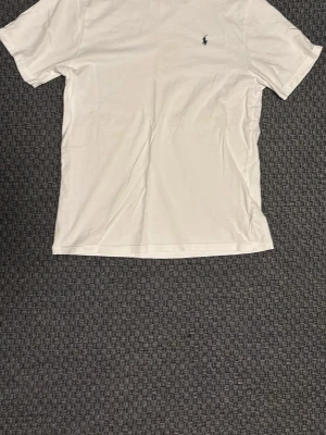 Vit t-shirt från Ralph Lauren - Klassisk vit t-shirt från Ralph Lauren med liten broderad logga på bröstet. T-shirten har rund halsringning och korta ärmar, perfekt för en clean och stilren look.