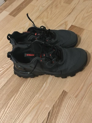 Svarta sneakers från Nike - Säljer ett par svarta sneakers från Nike med mesh- och syntetmaterial, robust sula och röda detaljer på snörningen. Skorna har rund tå och platt sula, perfekta för en sportig och avslappnad stil.