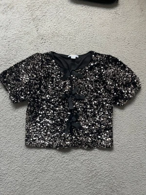 Svart paljettopp med rosetter - Tryck inte köp nu, hör av dig först! ❤️Glittrig svart topp täckt av paljetter med rosetter. Toppen är i nyskick då den endast är testad och aldrig använd Nypris: 350kr, priset kan diskuteras storlek: 146/152❤️