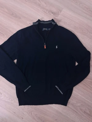 Mörkblå halvzip-tröja från Polo Ralph Lauren - Mörkblå långärmad tröja från Polo Ralph Lauren med halv dragkedja och klassisk broderad logga på bröstet. Tröjan har ribbade muddar och krage med randig detalj. Perfekt för en stilren och avslappnad look. Priset kan diskuteras!