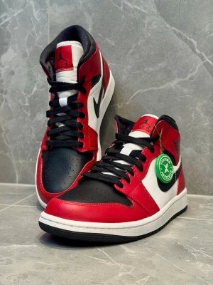 Nike Air Jordan 1 Chicago sneakers - Säljer ett par ikoniska Nike Air Jordan 1 sneakers i färgerna röd, vit och svart. Skorna har klassisk snörning, svart swoosh och rund tå. Tillverkade i skinn med hög siluett och autenticitetsbricka från StockX.
