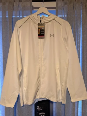 Vit vindjacka från Under Armour - Helt ny Windbreaker från Under Armour. Storlek M. Alla tags är kvar. Tveka inte vid att höra av er!