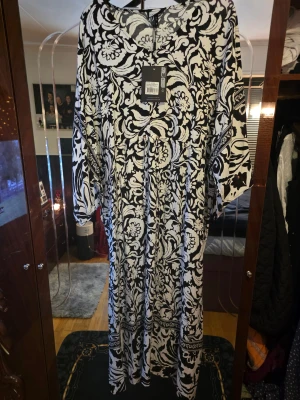 Svartvit långklänning från Gozzip - Långklänning från Gozzip i svartvitt blommigt mönster. Klänningen har v-ringning, vida trekvartsärmar och knytband i midjan. Tillverkad i mjuk viskoskvalitet som känns luftig och skön. Perfekt för dig som gillar statement-plagg med snygg passform.