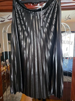 Plisserad glittrig långkjol från Only Carmakoma - Snygg svart plisserad långkjol från Only Carmakoma Curve med glittrig finish. Kjolen har ett elastiskt midjeband och skimrande tyg som ger en cool metallic look. Perfekt för dig som vill sticka ut med stil och gillar trendiga detaljer.