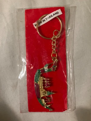 Nyckelring med thailändsk båt - Unik nyckelring med en detaljrik thailändsk båt i guld, grönt och rött. Båten har små tempelliknande detaljer och är fäst i en guldfärgad kedja. Perfekt accessoar för dig som gillar färg och vill ha något annorlunda på nyckelknippan.