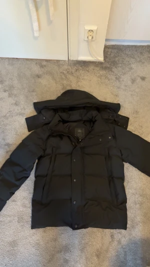 Canada Goose jacka - Helst byta mot en annan jacka i Xs. Pris kan diskuteras vid snabb upphämtning. Svart dunjacka från Canada Goose med Fusion-passform. Jackan har huva, dragkedja och knappar framtill samt ett snyggt svart märke på ärmen. Perfekt för kalla dagar med sin tjocka och quiltade design. Klassisk look och riktigt varm.