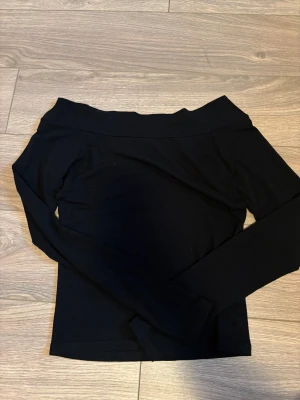 Svart offshoulder topp från BikBok - Svart offshoulder topp från BikBok i storlek M. Toppen har lång ärm och är figurnära med en bred kant upptill som ger en snygg offshoulder-look. Materialet är mjukt och stretchigt, troligtvis bomull eller polyester. Perfekt för dig som gillar stilrena och enkla plagg.