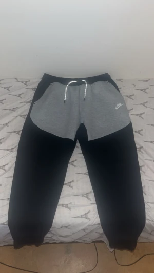 Nike mjukisbyxor XL svart/grå - Nike mjukisbyxor i storlek XL med svart ben och grå panel upptill. Snyggt Nike-logga på vänster sida och praktisk snörning i midjan. Sköna och stilrena, perfekta för chill eller träning. Tillverkade i mjukt bomullsmaterial för maximal komfort.