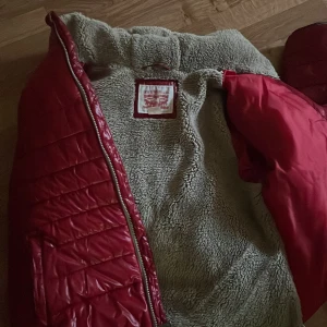 Röd pufferjacka med teddyfoder - Säljer en supermysig röd pufferjacka med teddyfoder. Den har en glansig yta och är perfekt för kalla dagar. Jackan har en dragkedja framtill och en skön huva. Perfekt för vintern och hösten när du vill hålla dig varm och snygg!