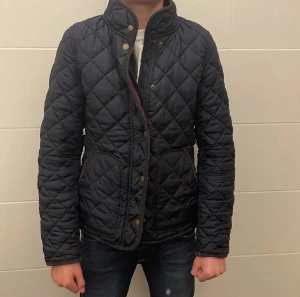 Svart quiltad jacka från GANT - Säljer en svart quiltad jacka från GANT i storlek S. Jackan har hög krage, tryckknappar och dragkedja framtill. Den är tillverkad i polyester och har ett snyggt rutmönster. Perfekt för höst och vinter när du vill ha en stilren look. Pris kan diskuteras!