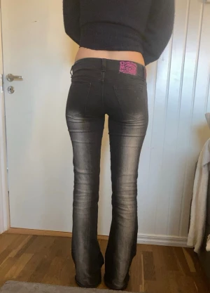 jens från cheap monday - Säljer ett par svarta bootcut jeans från Cheap Monday med låg midja och coolt rosa logopatch bak. Jeansen har slitna detaljer och en snygg tvätt som ger dem en edgy vibe. Passar dig som gillar en smal passform upptill och utsvängda ben.  Storlek w28-29 längd 34 