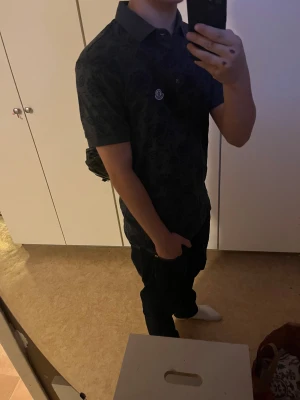 Mörkblå Moncler piké - Snygg mörkblå pikétröja från Moncler i storlek S ( passar definitivt M )  blommigt mönster över hela skjortan. Använt ungefär 2 gånger, pga storlek. Något du undrar eller pris diskussion, säg bara till! 