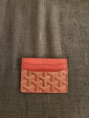 Röd plånbok - Snygg röd plånbok från med klassiskt grafiskt mönster i vitt och beige. Plånboken har flera fack för kort och är tillverkad i skinn med  ikoniska tryck på både fram- och baksida. Perfekt för dig som gillar exklusiva accessoarer med unik design.