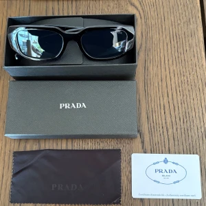 Svarta solglasögon från Prada (Okulary)  - Snygga svarta solglasögon från Prada. Modellen är Okulary och levereras med originalbox, putsduk och äkthetskort. Säljer dem då jag inte riktigt kände att dem var för mig! 