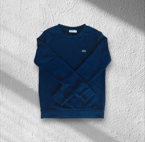 Marinblå sweatshirt från Lacoste - Snygg marinblå sweatshirt från Lacoste med klassisk rund hals och det ikoniska krokodilloggan broderad på bröstet. Tröjan har långa ärmar och ribbade muddar vid ärmslut och nederkant. Perfekt för en chill och stilren look.