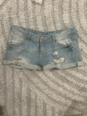 Ljusblå jeansshorts med slitningar - Snygga lågmidjade jeansshorts. Säljer för att dom är för små. Använt några gånger men ser helt nya ut. 