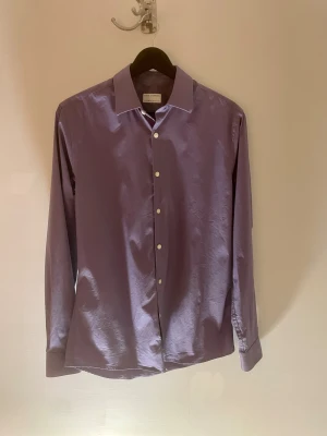 Lila skjorta Tiger of Sweden extra slim - Snygg lila skjorta från Tiger of Sweden i extra slim fit. Klassisk krage, långärmad och med vita knappar framtill samt på manschetterna. Skjortan är tillverkad i mjuk bomull och har en stilren, modern look som passar dig som gillar minimalistisk stil.