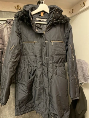 Marinblp parkajacka från Tiger of Sweden - Marinblå  parkajacka från Tiger of Sweden med huva och snygg pälsdetalj. Jackan har flera dragkedjor, stora fickor och markerad midja med resår. Perfekt för kalla dagar och har en stilren look som funkar till många outfits.