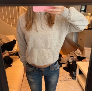 Ljusgrå hoodie med huva och magficka - Säljer en ljusgrå hoodie med klassisk huva och snörning. Tröjan har en stor magficka framtill och ribbade muddar vid ärmslut och nederkant. Perfekt för chill dagar och enkel att matcha med jeans eller mjukisbyxor.