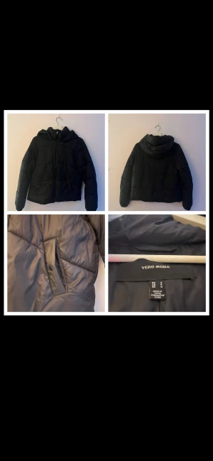 Svart pufferjacka från Vero Moda - (En knapp är borta vilket gör att man inte kan stänga en ficka).           Svart pufferjacka från Vero Moda med huva och dragkedja framtill. Jackan har två fickor med knappstängning och quiltade detaljer. Perfekt för kyliga dagar och har en modern, lite kortare passform.