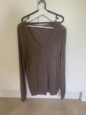 Brun v-ringad tröja - Brun långärmad tröja från med v-ringning. Mjuk och tunn finstickad. Sitter normalt och har ribbade muddar vid ärmslut och nederkant. Enkel och stilren design som funkar till många outfits. Använd 1 gång