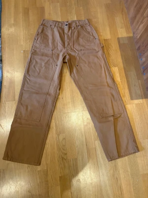 Carhartt Double Knee i brun - Ett par carhartt double knees i brun som är använda 1 gång. Har använts och tvättats 1 gång. Inga fel med dem. Har ganska straight baggy passform