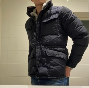 Moncler kavaj/vinterjacka - Snygg mörkblå dunjacka från Moncler med hög krage, flera fickor med lock och dragkedja samt tryckknappar framtill. Jackan har Moncler-logga på ärmen och är tillverkad i glansig polyester.✅ Perfekt för kalla dagar. Skriv privat för fler bilder eller med bild på✅ 