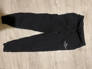 Svarta mjukisbyxor Peak Performance - Svarta mjukisbyxor från Peak Performance med broderad logga på benet. Byxorna har snörning i midjan och ribbade muddar vid bensluten. Perfekta för chill eller träning, mjukt material och klassisk look.